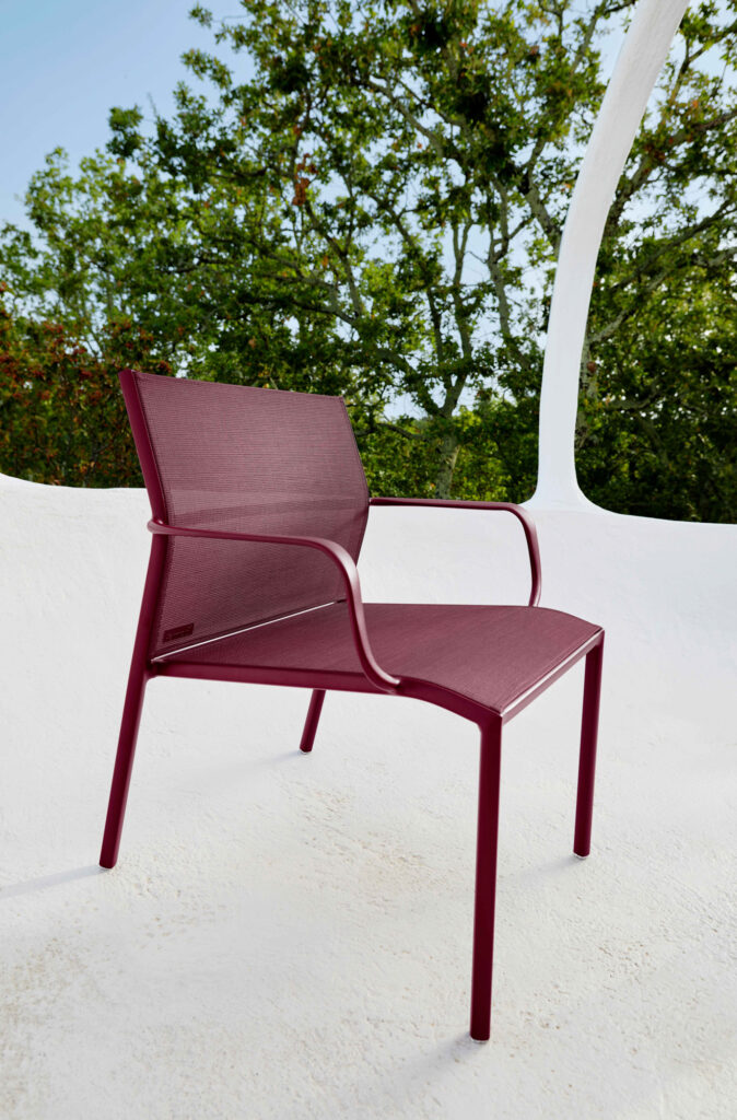 Un Fauteuil bas Cadiz marron avec un siège et un dossier en maille est placé sur une surface blanche à l'extérieur avec des arbres en arrière-plan.