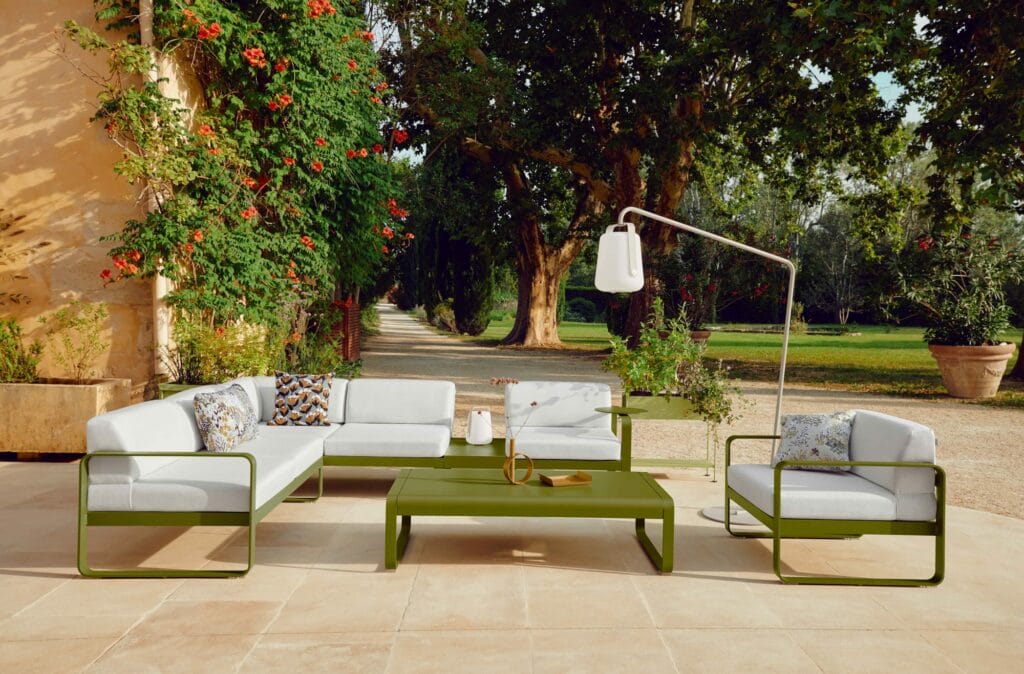 Mobilier de patio extérieur, comprenant des canapés et une table basse Bellevie, installés dans un jardin arboré et fleuri sous un ciel dégagé.