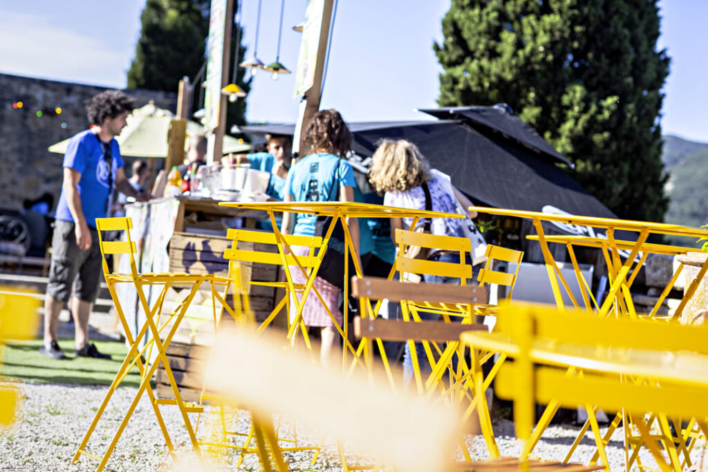 Un groupe de personnes debout près d’un bistro Mange debout rempli de chaises jaunes.