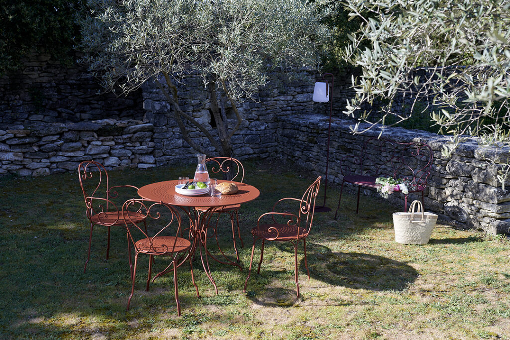 Une table Fauteuil 1900 et des chaises Fauteuil dans une cour avec un olivier.