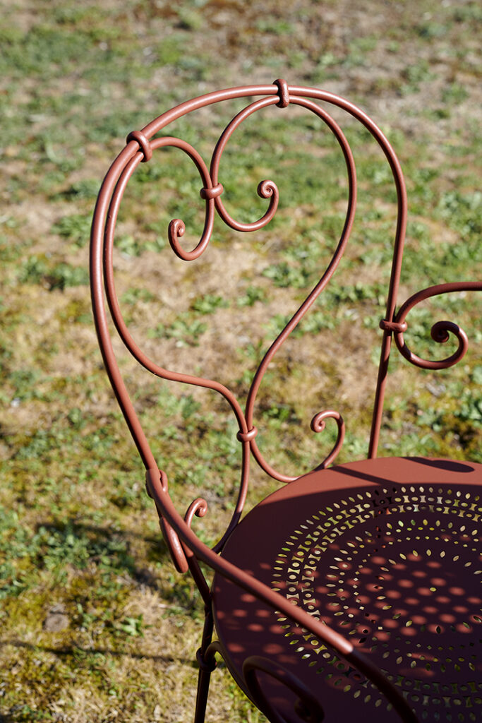 Une chaise Fauteuil 1900 rouge dans un espace herbeux.