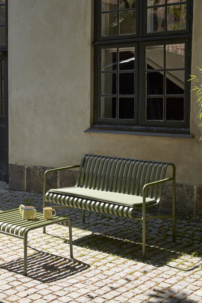 Un banc Palissade gris ciel avec un Coussin d'assise dans une rue pavée.