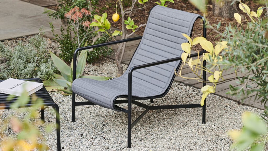 Un Coussin matelassé noir et gris pour fauteuil dossier haut Chaise longue Palissade dans un jardin, avec des coussins matelassés.