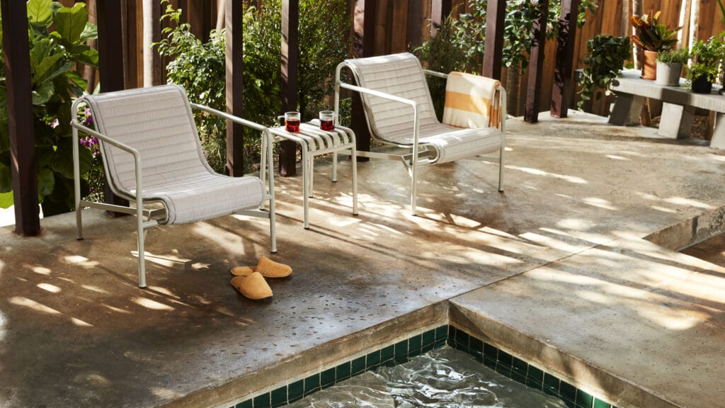Une terrasse en bois avec deux chaises Coussin matelassé pour fauteuil bas Palissade et une table devant une piscine.
