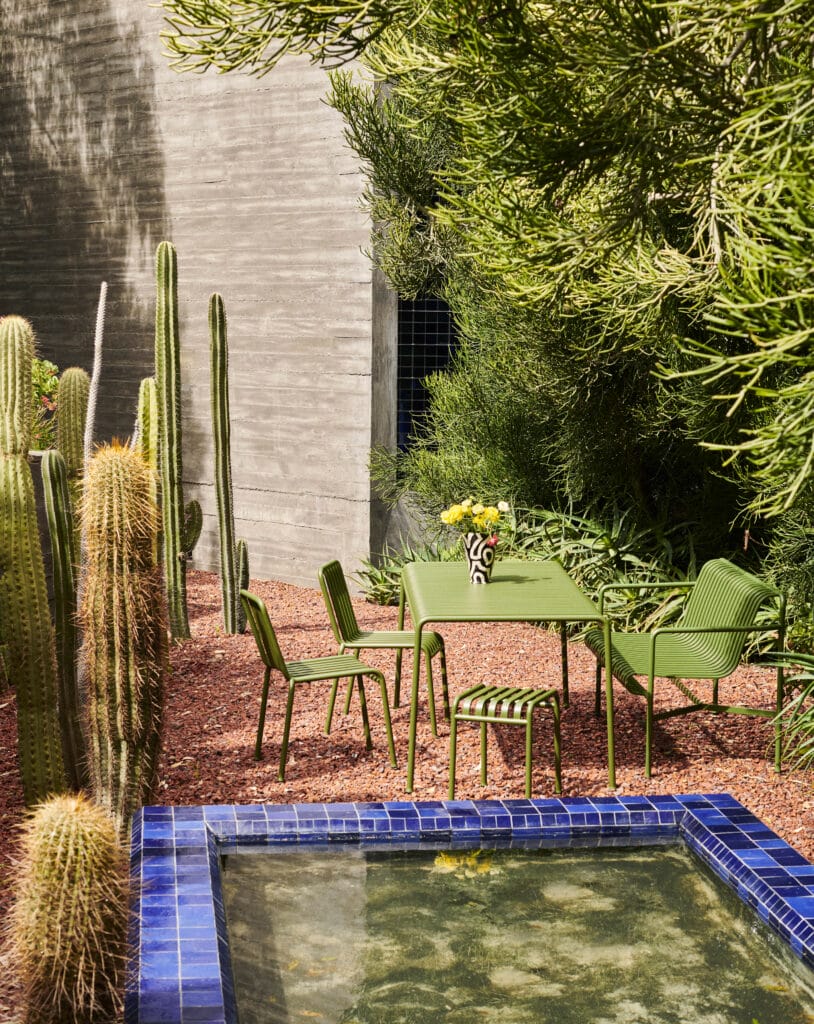 Un Tabouret Palissade vert et des chaises dans un jardin avec des cactus, entouré de palissade.