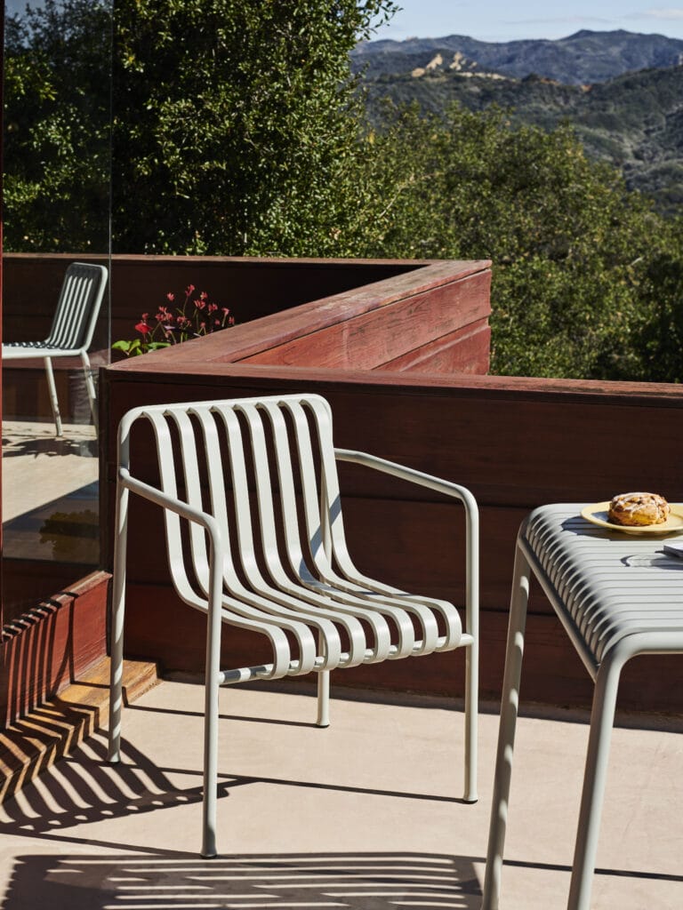 Une table vert olive et des fauteuils sur un patio avec vue sur les montagnes.