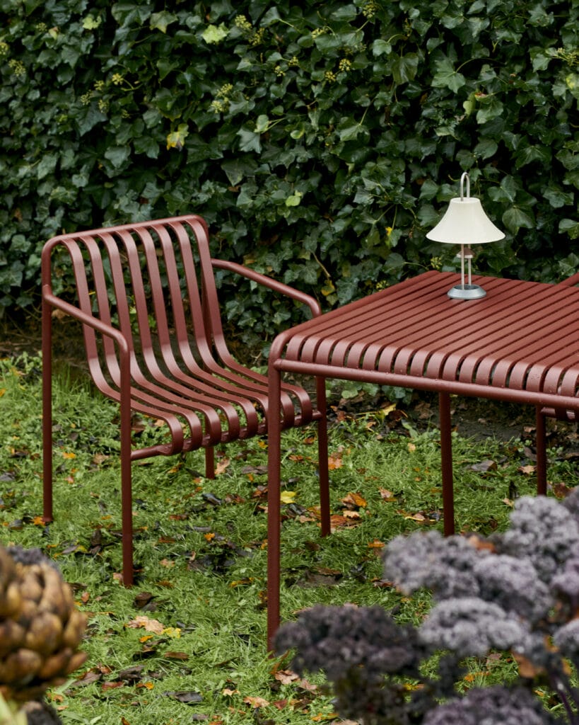 Une Table Palissade rouge, 170 x 90 cm et des chaises avec une palissade dans un jardin.