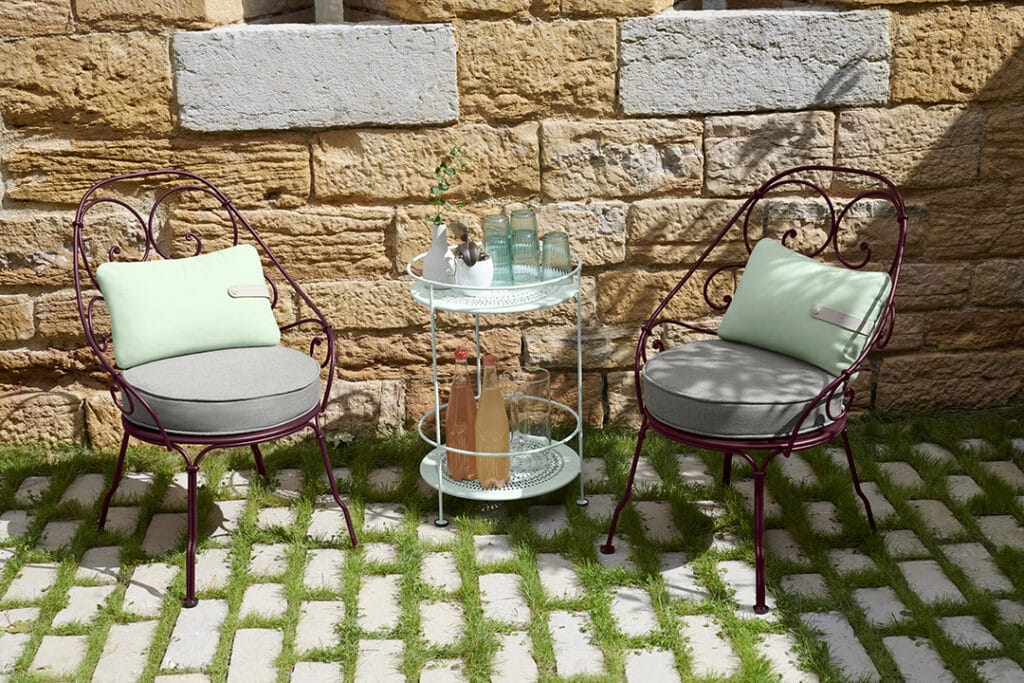 Une table Guéridon Guingette et deux chaises disposées devant un mur en pierre.