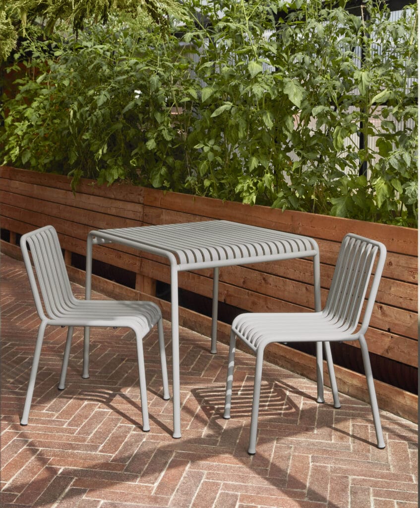 Deux chaises et une table carrée Palissade sur un patio en brique avec une palissade entourant l'espace.