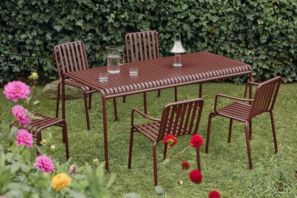 Une Table carrée Palissade avec des chaises carrées dans un jardin entouré de fleurs.