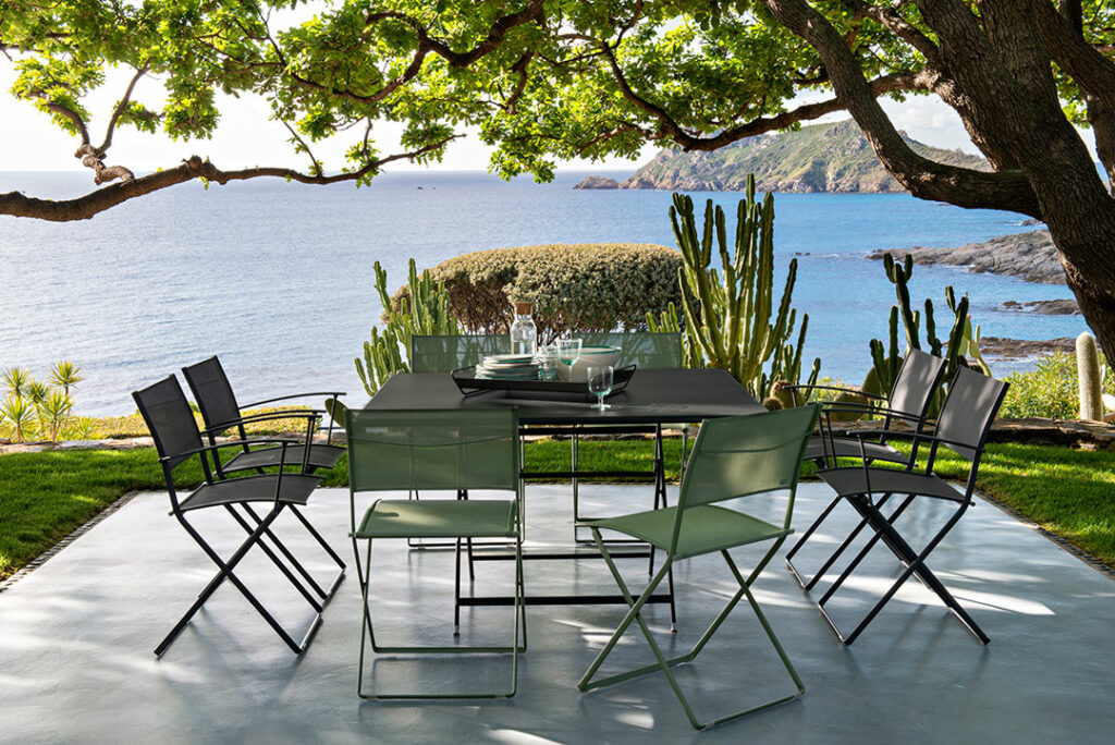 Une Table pliante carrée Caractère et des chaises sur un patio avec vue sur l'océan.