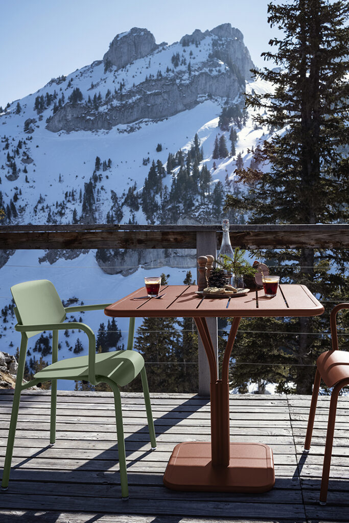 Deux chaises et une Table carrée Luxembourg, pied central sur une terrasse avec des montagnes enneigées en arrière-plan.