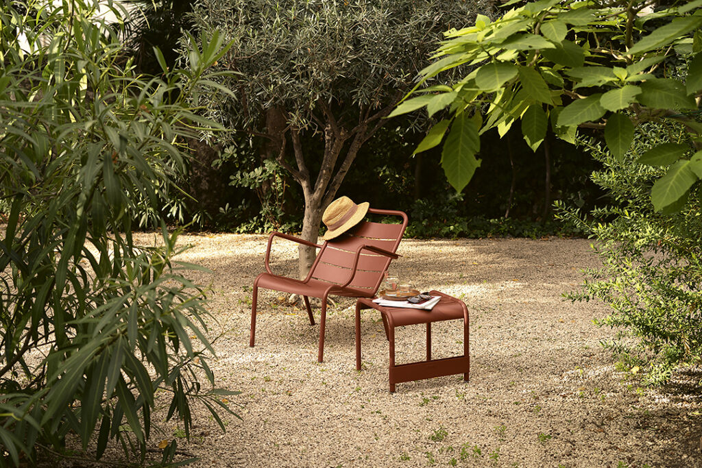 Une chaise Fauteuil bas Luxembourg rouge est posée dans la terre à côté d'un chapeau.