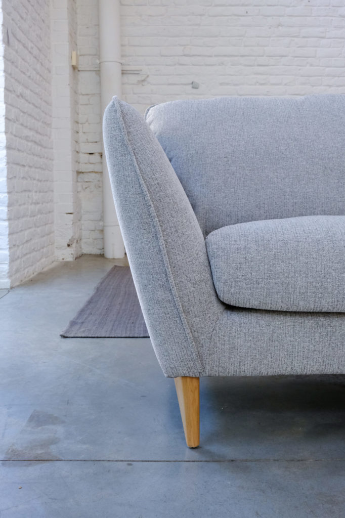 Un canapé gris Canapé Stella avec des pieds en bois dans une pièce blanche.