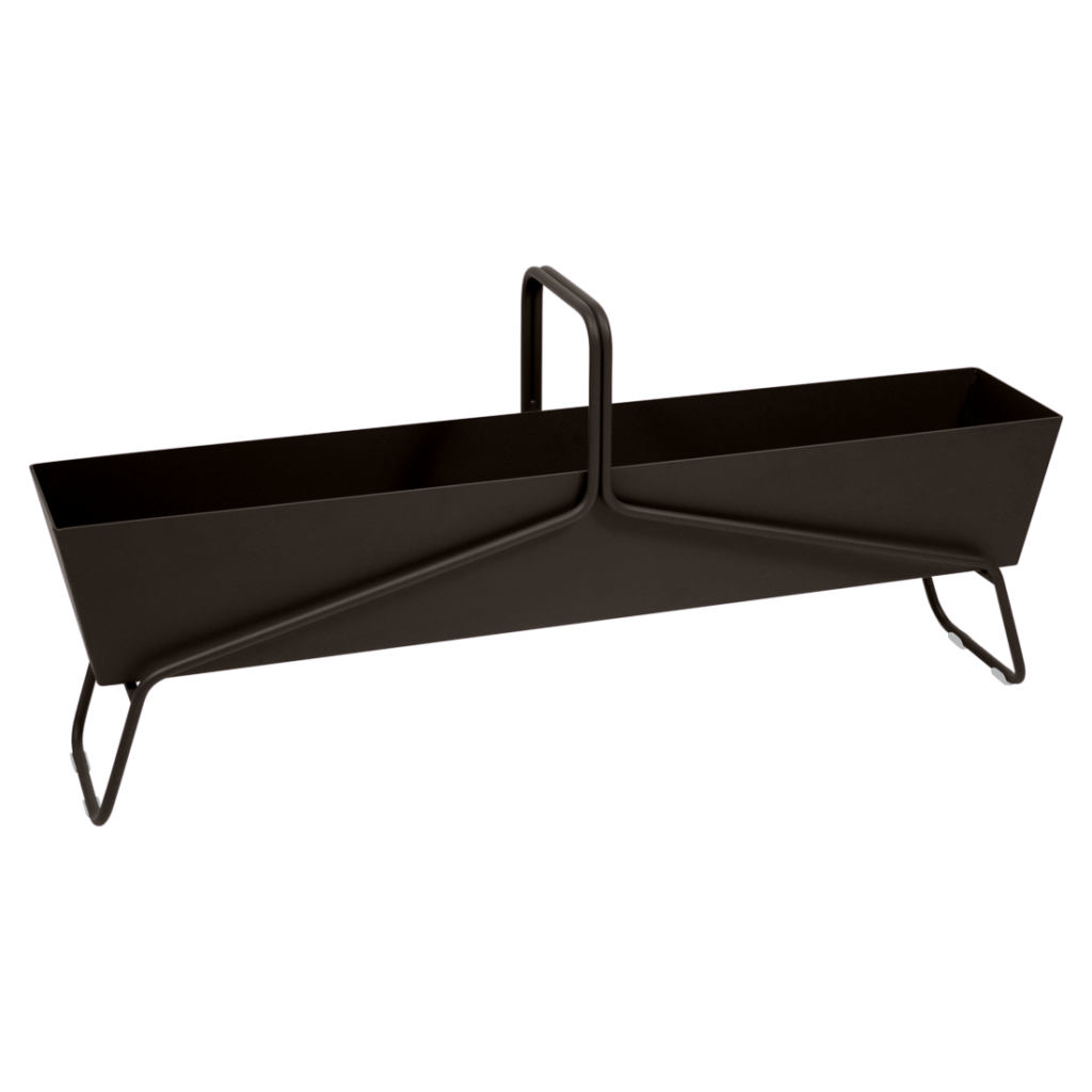 La Jardinière longue Basket est une jardinière élégante en métal noir avec une poignée centrale et des pieds inclinés, présentée sur un fond violet clair uni.