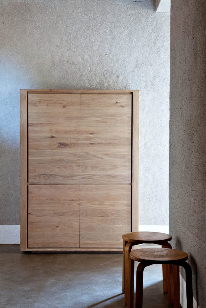 Une armoire en bois dans une pièce à côté d’un tabouret.