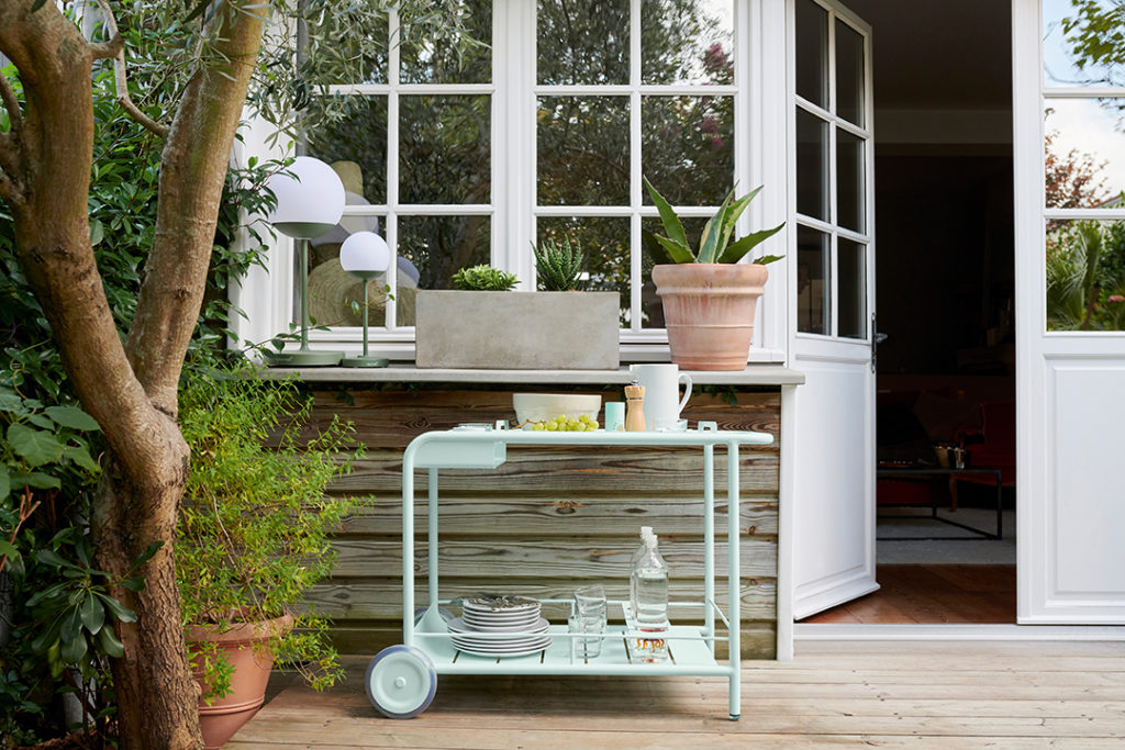 Un chariot vert sur une terrasse en bois avec des plantes en pot.