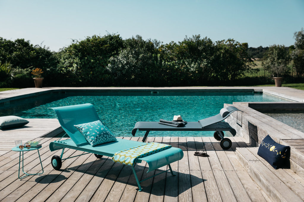 Une chaise longue bleue sur une terrasse en bois à côté d'une piscine.