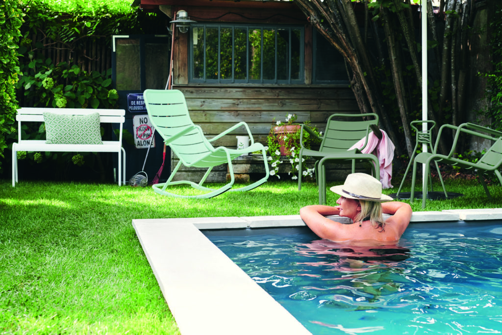 Fauteuil de jardin rocking chair luxembourg en aluminium laque tons vert autour d'une piscine avec une femme et petite cabane de jardin