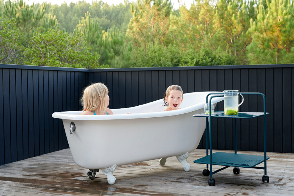 Deux filles assises dans une baignoire sur une terrasse en bois.