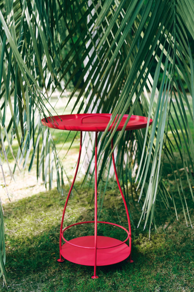 Une table rouge dans l’herbe à côté d’un palmier.
