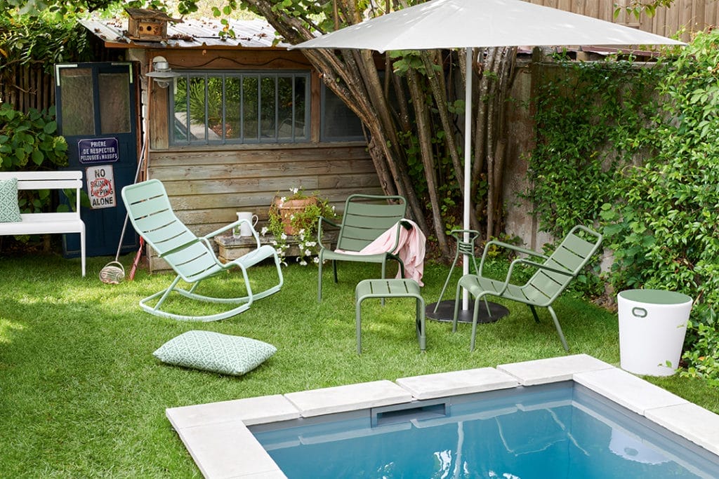 Fauteuil bas luxembourg en aluminium laque couleur cactus vert autour d'une piscine dans un jardin avec un parasol