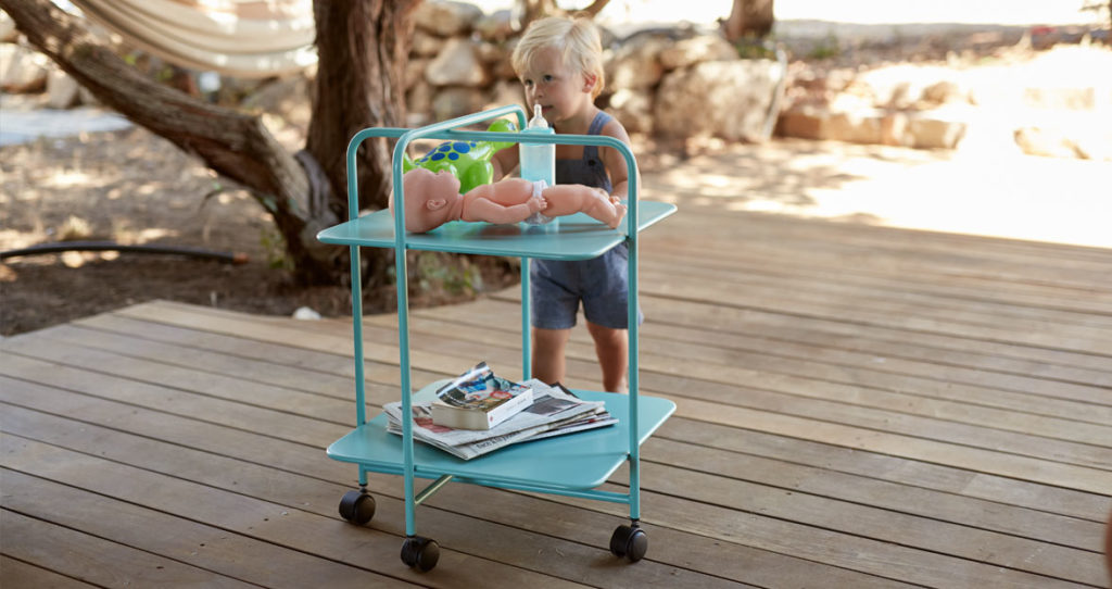 Un enfant est debout sur une terrasse en bois avec un chariot bleu.