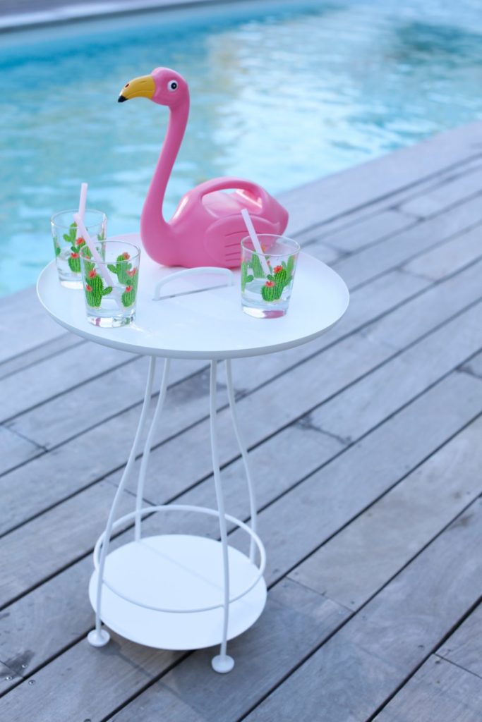 Un flamant rose assis sur une table au bord d’une piscine.