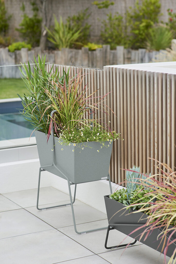 Deux hauts paniers Jardinière haute sur un patio au bord d'une piscine.