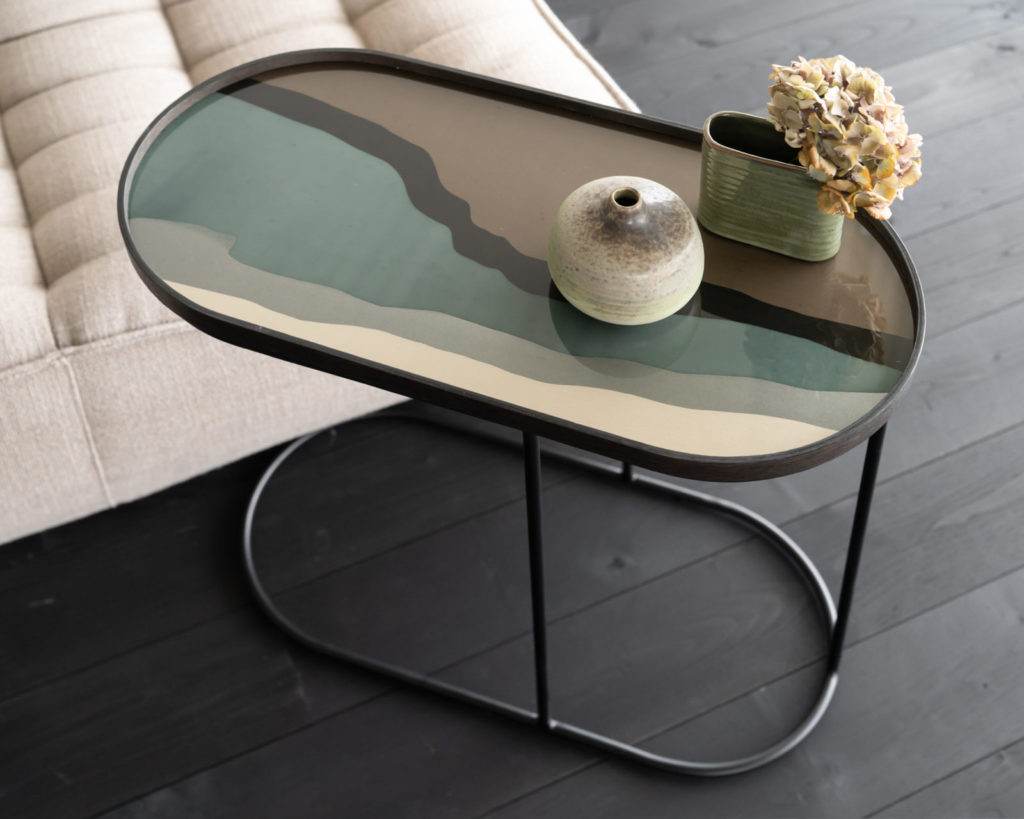 Une table d'appoint Plateau ovale/oblong en verre Graphite Wabi Sabi Medium avec un vase en verre sur le dessus.