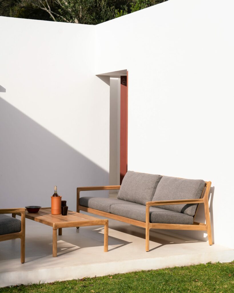 Un canapé en bois de teck situé dans un jardin avec un mur blanc.
