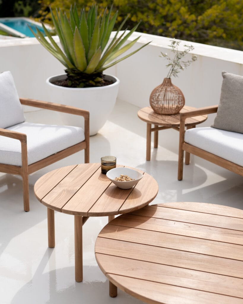 Une __Table basse de jardin Quatro__ en bois avec des chaises blanches et une plante en pot.