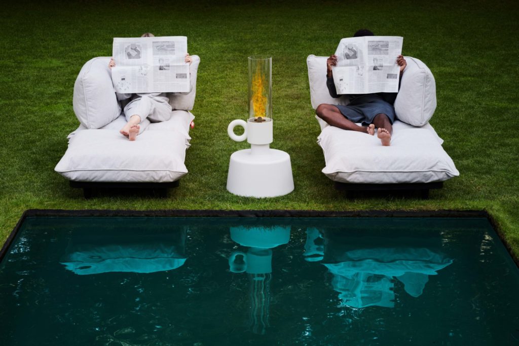 Deux personnes lisant un journal sur une chaise longue au bord d’une piscine.