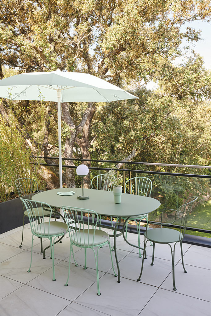 Une table et des chaises sur un patio avec un Parasol Shadoo vert.