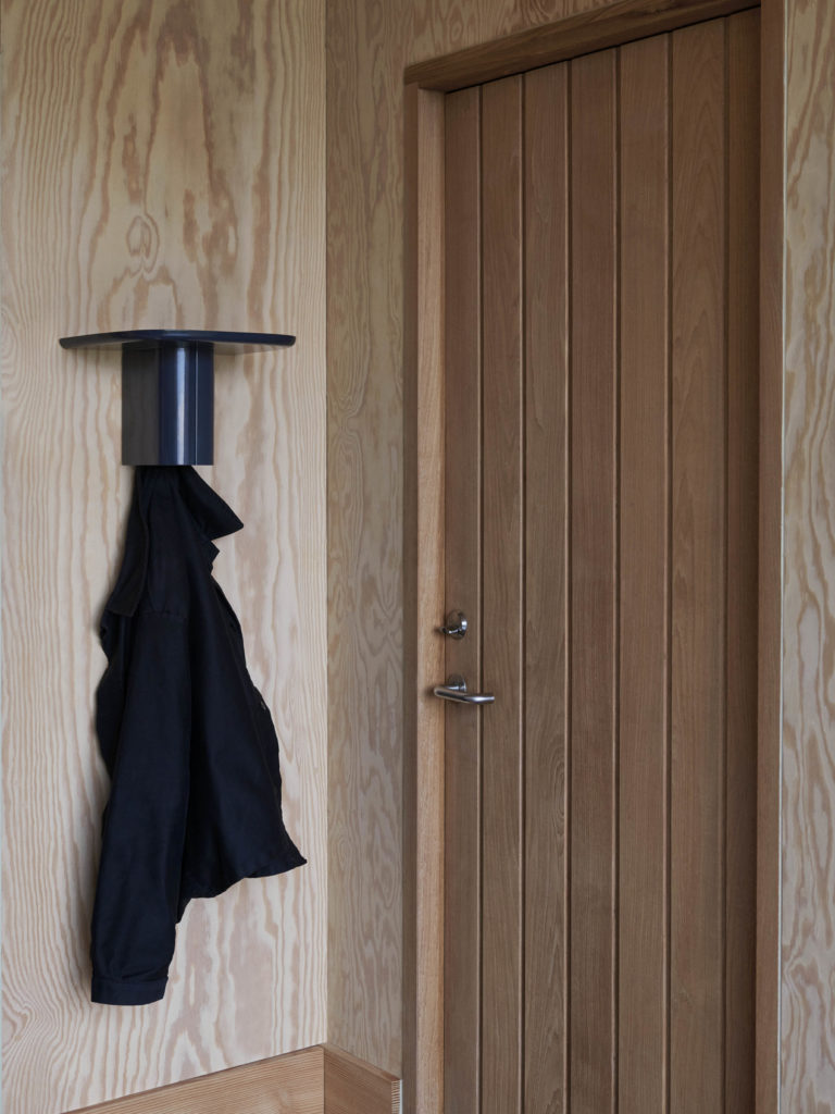 Etagère porte-manteau Korpus taille S en aluminium de la marque Hay à coté d'une porte en boisavec un manteau sur le porte-manteau