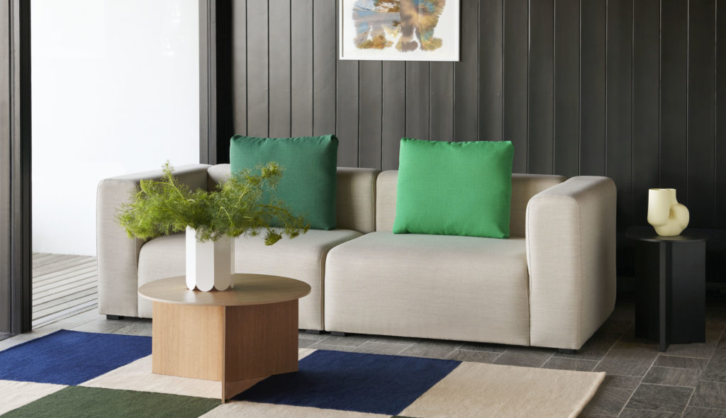 Un canapé dans un salon avec des coussins verts et bleus accompagné d'une table d'appoint ronde en bois fendu.