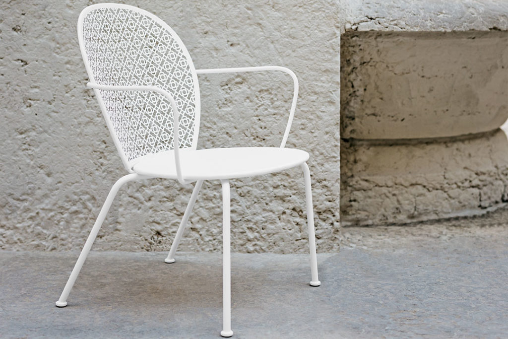 Une chaise longue fauteuil en coton blanc est placée devant un mur de pierre.
