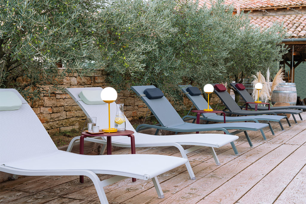Une rangée de chaises longues sur une terrasse en bois, comprenant un mélange de coussins Color Mix et des oreillers Appui-tête Color Mix pour plus de confort.