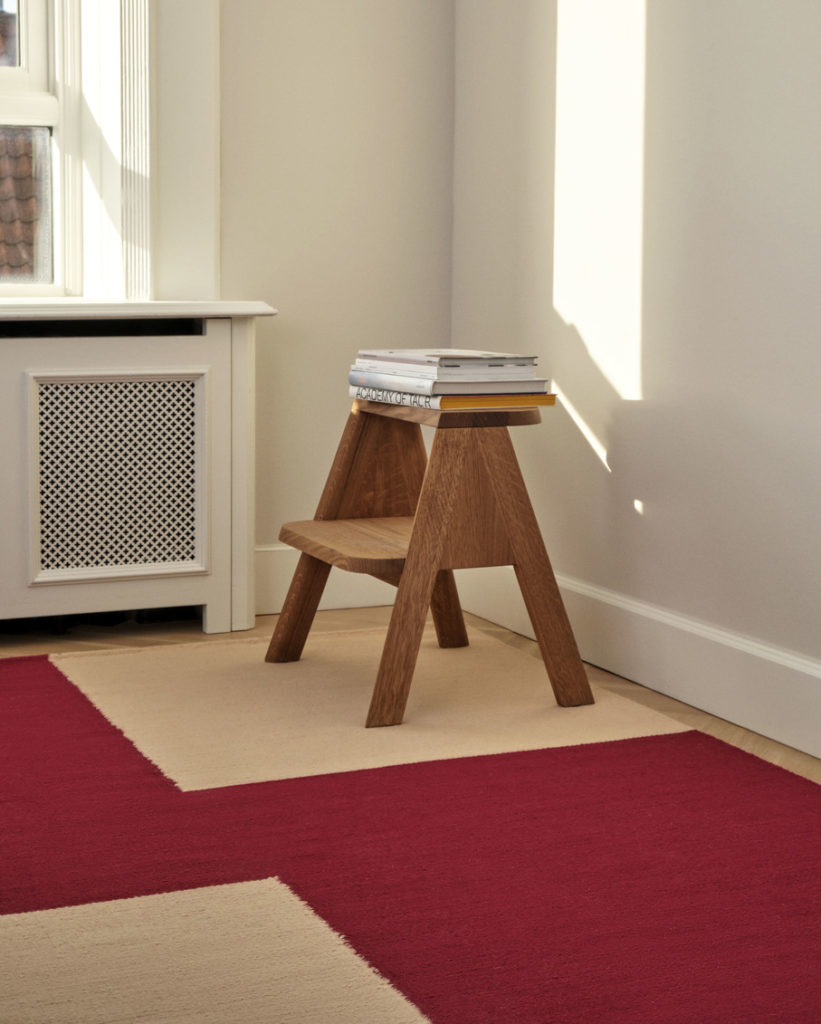 Tapis Ethan Cook en laine et coton de la marque Hay dans une pièce avec un escabeau en bois avec des livres sur le dessus dans les tons rouge beige
