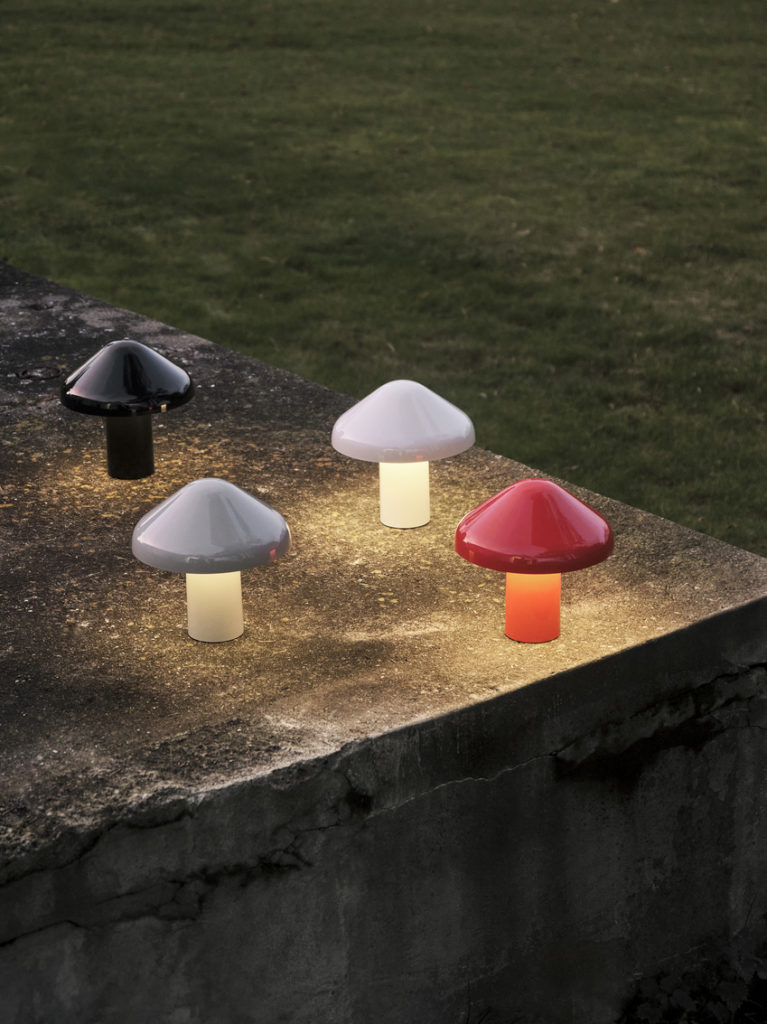Une Lampe portable Pao en forme de champignon rouge et blanc illuminant une dalle de béton.