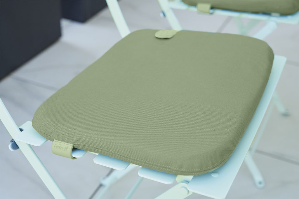 Une chaise Galette verte Bistro Color Mix repose sur une chaise pliante, ajoutant une touche de couleur à la disposition des sièges d'inspiration bistro.