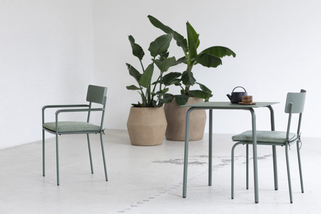 Au mois d'août, il y a une Table August carrée et deux chaises placées dans une pièce avec une plante en pot.