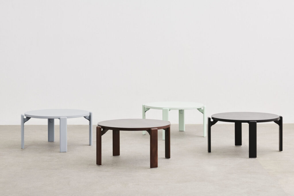 Quatre tables rondes, dont une table basse bleu ardoise et d'autres de couleurs et finitions variées, sont disposées sur un sol gris clair sur un fond blanc uni.