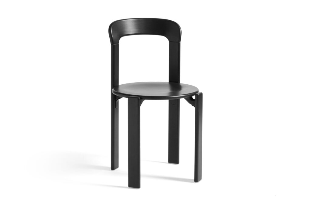 Une chaise minimaliste noire, rappelant le style Chaise Rey, présente un dossier incurvé et quatre pieds droits sur un fond blanc uni.