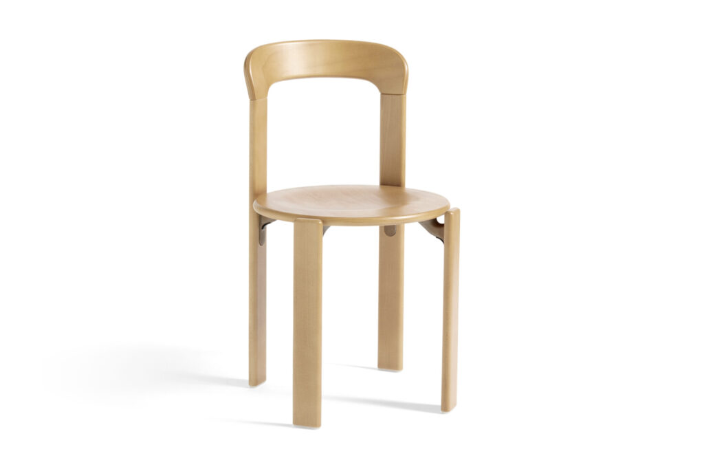 Une chaise en bois minimaliste, rappelant une chaise classique, présente un dossier incurvé et quatre pieds droits sur un fond bleu foncé et blanc.