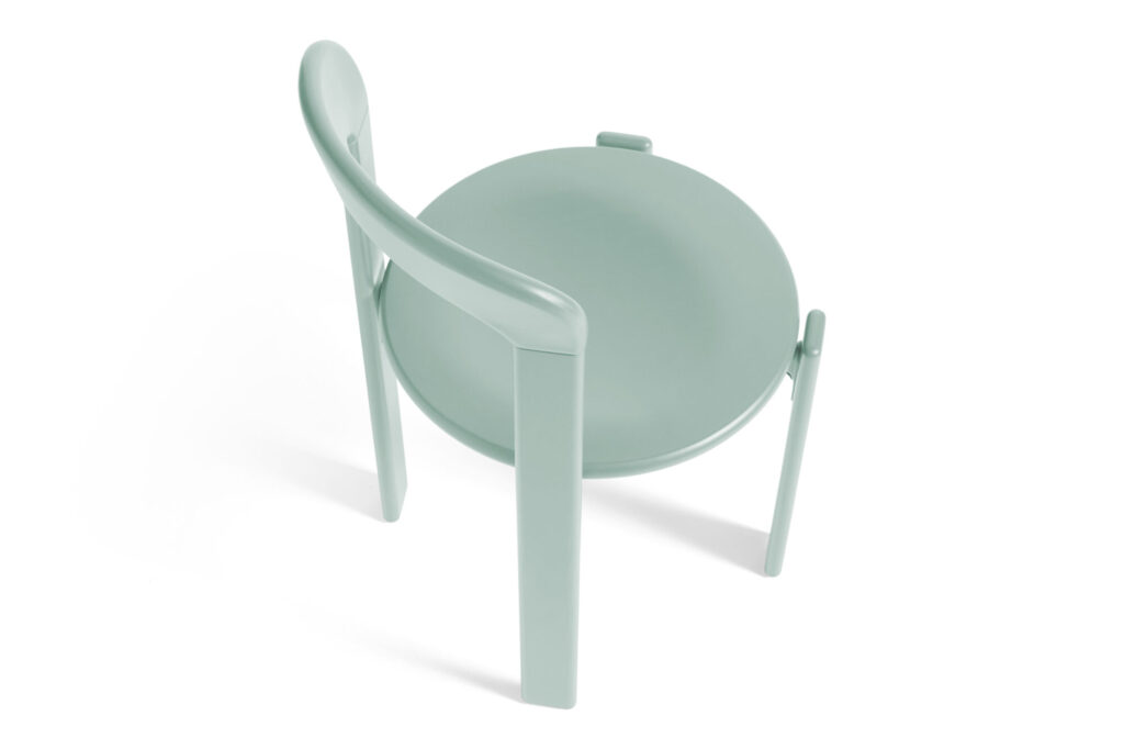 Une chaise à dossier rond vert menthe au design minimaliste se présente sur un fond blanc immaculé, subtilement contrasté par une teinte bleu profond qui ajoute de la profondeur et du caractère.