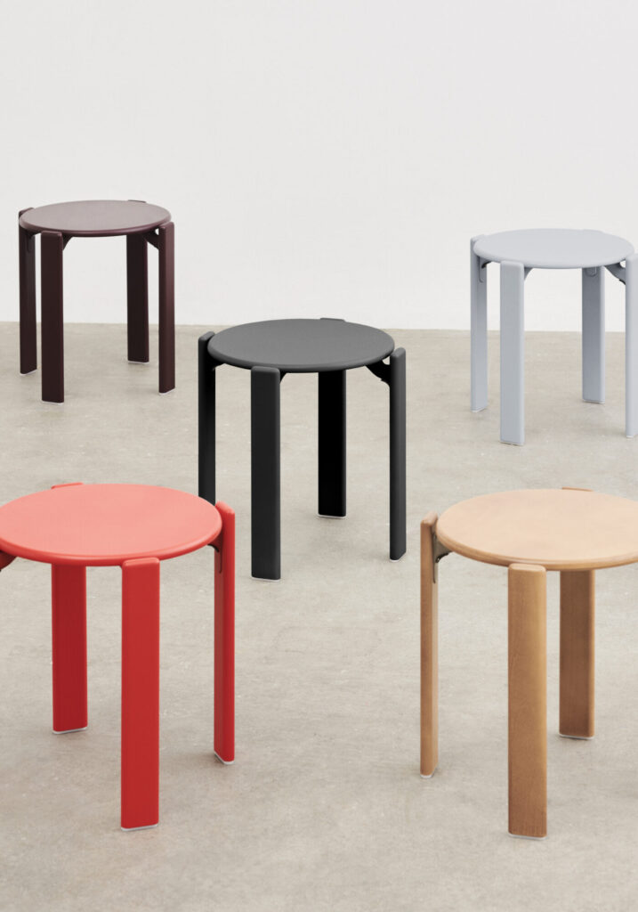 Cinq tabourets ronds, dont un élégant Tabouret Rey bleu ardoise aux côtés d'options rouge, noir, marron et beige, sont disposés sur un sol de couleur claire contre un mur blanc uni.