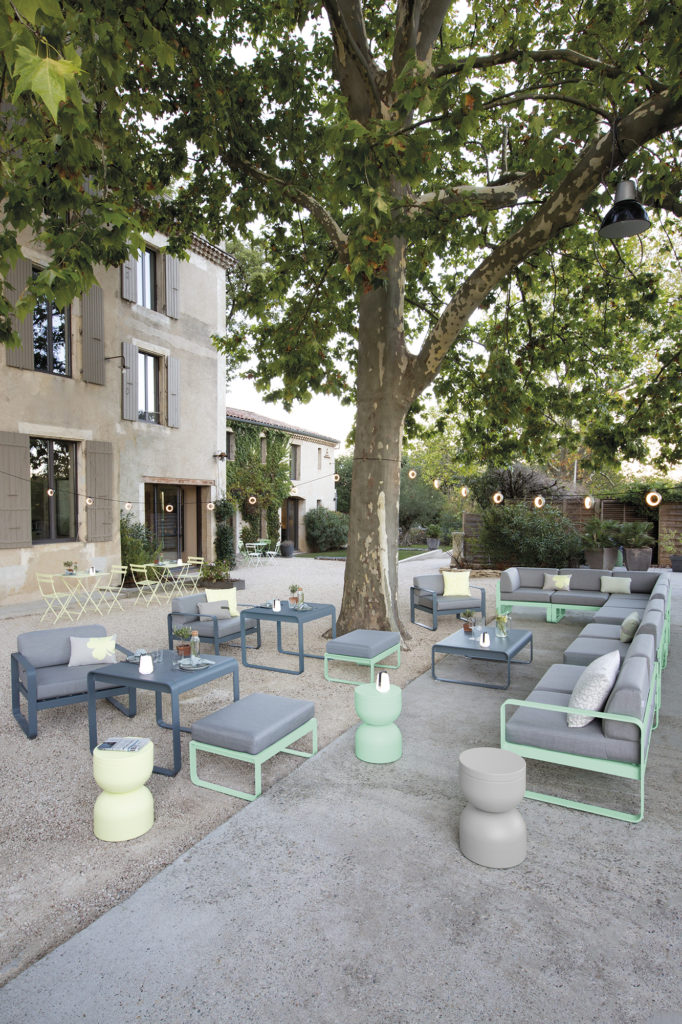 Pouf d’extérieur avec coussin et tables mi-hauteur dans un jardin et gravier soleil couchant