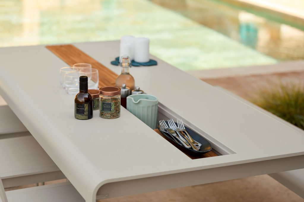 Table Bellevie avec rangement central pour couverts, poivrier et vinaigrette au bord de la piscine
