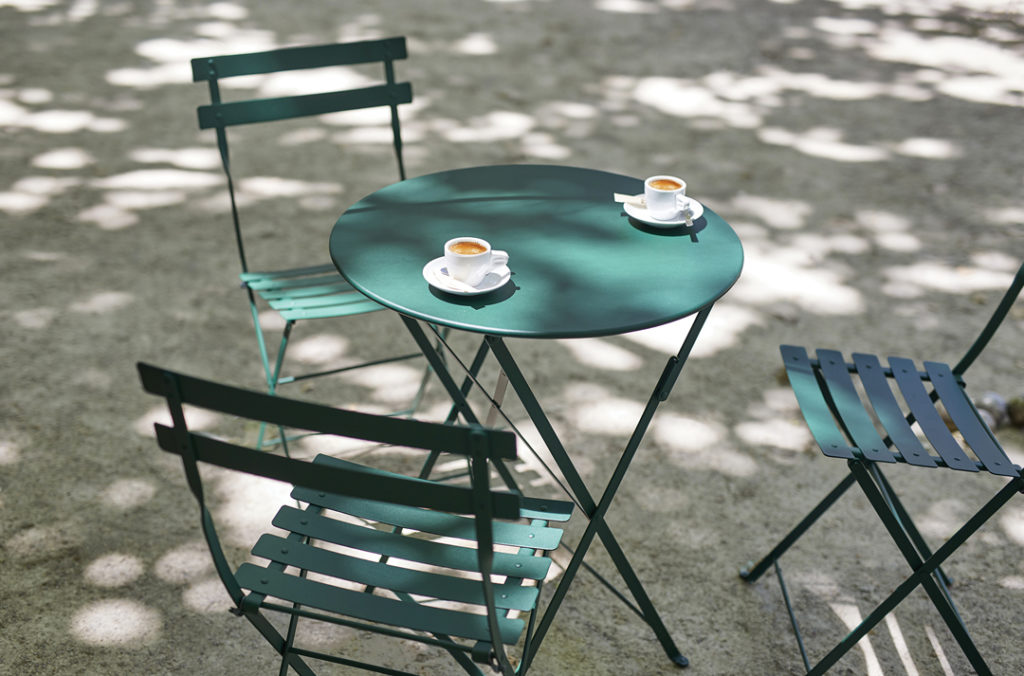Petite table d’extérieur fermob posée sur une piste de pétanque à l’ombre pour le café d’après-midi